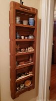 Full view of the tall narrow wooden curio shelf with various miniature crocks and souvenirs displayed on six shelves.
