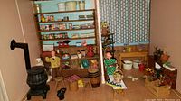 View of wooden store shelves, dolls, black stove and assorted miniature furniture and accessories in street scene vignette