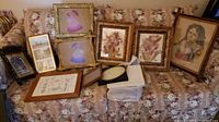 Image showing collection of framed artwork and empty frames arranged on floral couch, including dried flower pressed art, embroidered stitched art, Cincinnati photograph, and portrait.