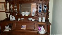 Wide view of various figurines and pitchers arranged on wooden hutch with mirror.