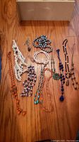 Photo showing full assortment of necklaces laid out on wood floor, various bead styles and colors visible