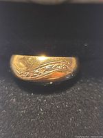 Close-up of ring showing engraved swirl pattern and three diamond chips on gold band