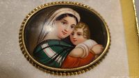 Close-up of brooch showing detailed hand painted mother and child on porcelain within gold tone frame