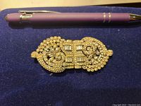 Front view of the Art Deco style brooch with paste diamond detailing placed next to a pen for scale.