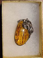 Brooch placed in a cushioned jewelry box showing the detailed silver vine and leaf design wrapped around polished Baltic amber with natural inclusions.