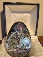 Glass paperweight with rainbow cascade design inside, shown in original display box from an angled front view.