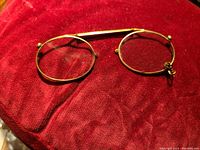 Top-down photo of round antique gold tone spectacles on red fabric background showing wire detail and chain attachment loop.