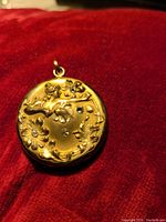 Front of gold tone round locket pendant with floral design and 4 clear rhinestones embedded in flowers.