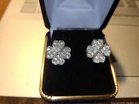 Pair of silver tone four leaf clover clip-on earrings studded with clear rhinestones, displayed in a black velvet box insert.