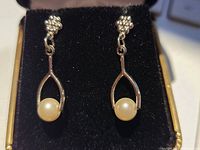 Pair of silver tone wishbone shaped earrings with faux pearl on black fabric background.