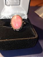 Front angle of the sterling silver ring with pink stone inside a black velvet ring box showing the detailed scalloped bezel.