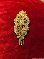 Clear front view of antique hair pin showing detailed floral and foliage design with clear paste stones on red velvet background