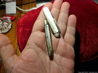 Photo shows two small pocket knives resting on a hand, highlighting mother of pearl handles and size comparison.