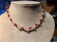 Front view of the vintage glass bead necklace displayed on a beige bust, showing alternating red and clear glass beads with sparkle.