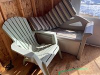 Resin Muskoka-style chair alongside resin storage bench in shed, showing worn condition and cushion on bench.
