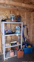 Photo showing shelving with gas cans (large and small), battery charger, washer fluid, oil, boxed remote car starter and sway control bar