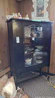 Front view of dark wood china cabinet with glass door. Cabinet contains multiple pieces of decorative ceramics and glassware, which are not included in the lot. Cabinet shows some surface scratches and wear.
