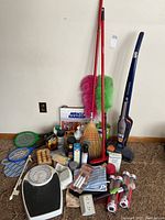 Full lot including vacuum, brooms, dusters, scale, flyswatters, cleaners, solar lights and other household items arranged on floor against wall