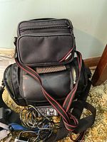 Compact and larger camera bags with shoulder strap and power cords displayed on carpeted floor.