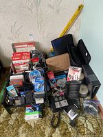 Photo showing various Canon printer ink packs, telephones, storage racks, binders, blank CDs, and assorted electronic accessories grouped together.