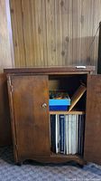 Front view of wood cabinet with doors open, showing internal shelf and vinyl records inside.