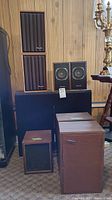 View of all speaker sets displayed in a room with wood paneling background, showing different sizes and brands.