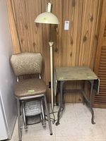 Photo showing the stenographer table, floor lamp, and vintage step stool chair arranged near a wall with wood paneling, tiled floor.