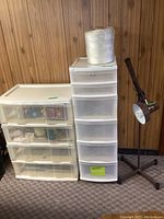 Photo showing two plastic storage drawer units and a large cone of white nylon string on top of one, with an adjustable work lamp on a stand beside them.