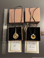 Two necklaces in original gift boxes, each with a certificate next to a ruler for size reference.