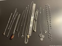 Top view of the 12 necklaces arranged alongside a ruler to indicate length and detail; various pendant designs and chain styles visible.