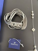 Photo showing Swarovski multi-wrap grey leather bracelet with crystals, Swarovski tag, and silver-tone necklace with white pearls flower embellishments