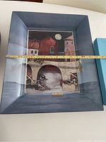 Front view of the porcelain wall mural featuring "The Red House" framed in blue, with measuring tape showing size.