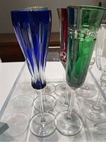 Colored champagne flutes in blue, green, and red with intricate cut designs and clear stems.