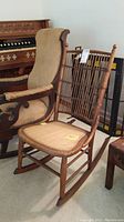 Full view of the antique wooden rocking chair showing wooden frame, spindle backrest, and woven cane seat.