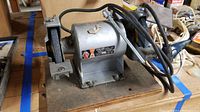 Full view of the Ashland bench grinder showing the grinder mounted on a wooden surface with power cord coiled on top.