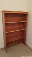 Front angled view of wooden bookcase showing three shelves and top trim