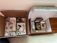 Two boxes containing various pins, clip-on earrings, and beads in multiple compartments.