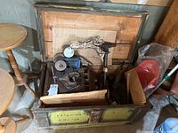 Wooden crate open revealing various metal and woodworking tools inside including a vise and sander.