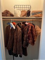 Full view of fur wraps hanging on rack with fur hats and slippers on top shelf