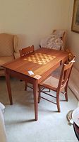 Full side-angle view of the rectangular wooden chess table with two chairs placed around it, showing the varnished wood finish and table dimensions.
