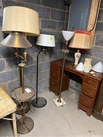 Four floor lamps and a ceramic table lamp grouped near wood desk in basement with visible soiling and tarnish