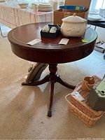 Round mahogany table with leather-like top, drawer partially open, and visible scratches.