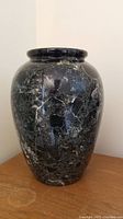 Front view of black marble vase with white marbling, showing classic rounded vase shape placed on wooden surface