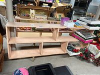 Front angled view of the light pink painted bookshelf with multiple open compartments, standing in basement with various boxes and decorations around it.