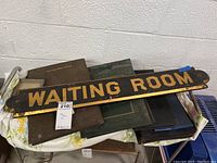 Photo showing multiple vintage photo albums stacked, with a wooden 'WAITING ROOM' sign placed on top.