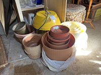 Various plastic and terracotta planters stacked and placed together, including different sizes of round terracotta and brown plastic pots along with a yellow electronic insect control unit.