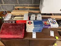 Full overview of all items in the lot displayed on a table showing the Rally IV TV computer game, bridge and duplicate boards, software boxes for PrintMaster and PrintShop 2.0, and two computer speakers.