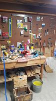 Full view of workbench with assorted tools, cleaning supplies, and hardware spread across the surface and shelves underneath