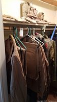Full view of several tan military jackets, pants, and camouflage shirt hanging in a closet.