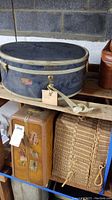 Photo of blue oval hat box, brown suitcase, and woven basket on wooden surface in basement